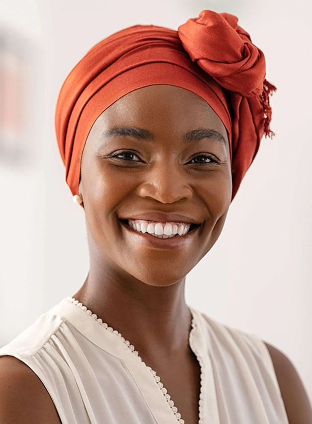 Smiling woman wearing orange head wrap in professional dental office portrait setting.