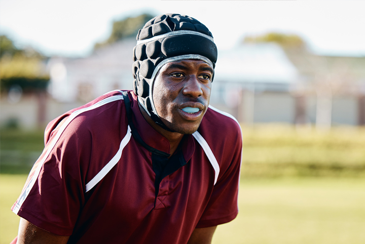 Male athlete wearing maroon sports jersey and helmet on outdoor grass field.