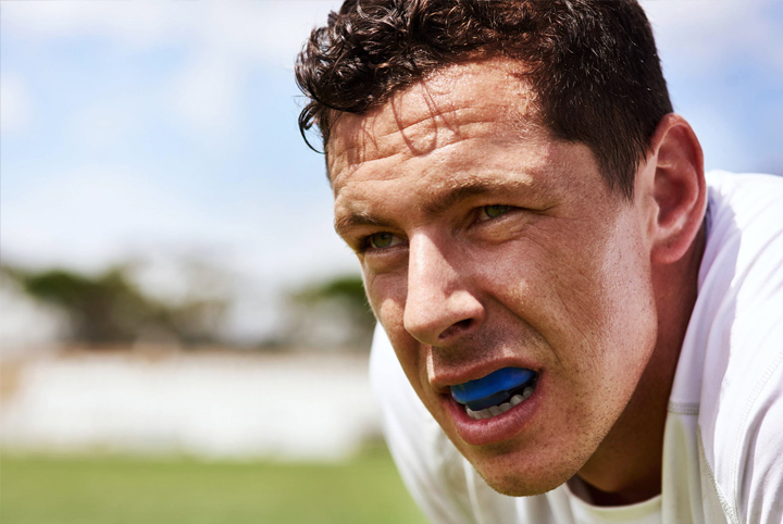 Athlete wearing blue mouthguard outdoors on sports field during daytime.