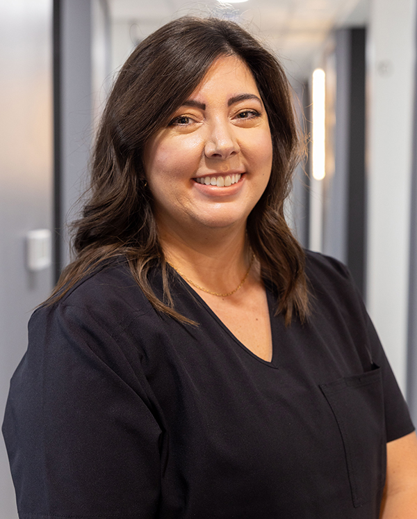 Woman in dark scrubs smiling at camera in dental office setting.