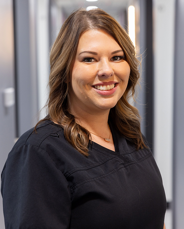 Woman in black scrubs smiling at camera in modern dental office setting.