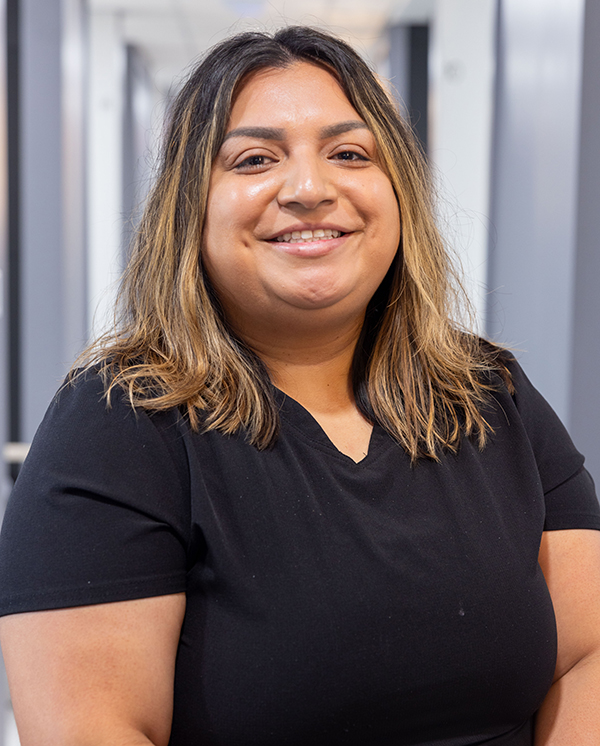 Woman smiling at camera in black shirt, professional headshot in dental office setting.