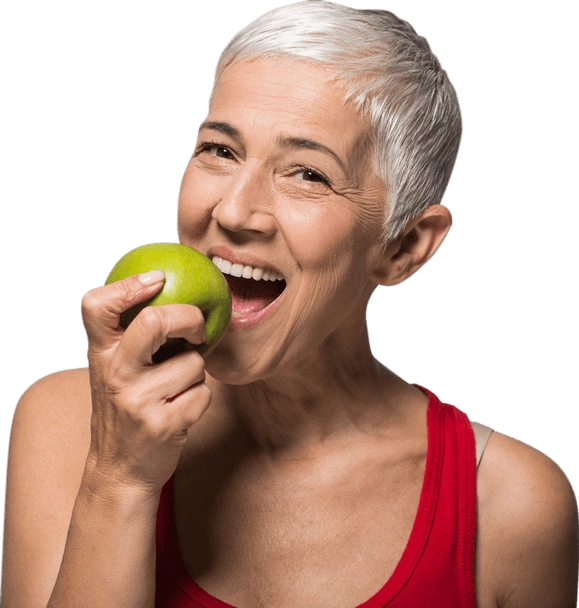 Mature woman in red tank top biting green apple, smiling against white background.