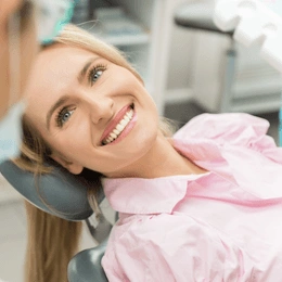 Happy woman in pink shirt smiling at dental office chair during checkup.