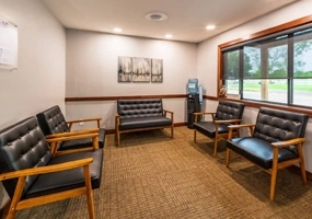 Modern dental waiting room with comfortable seating, warm lighting, and large windows.