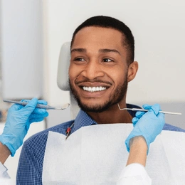 Smiling man receiving dental examination from dentist wearing blue gloves in clinical setting.
