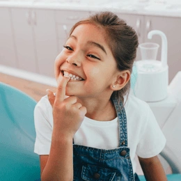 Young girl brushing teeth in bathroom sink, smiling at camera, dental care setting.